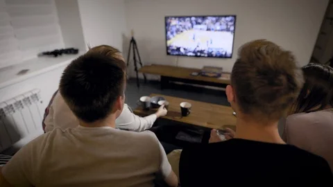 Young people sitting on settee and watching TV Stock Footage 99096908
