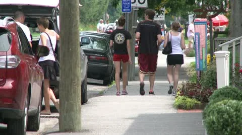 Young people walking down the sidewalk with cars parked along the road Stock Footage 10771765
