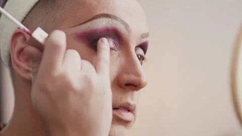 Young performer in drag queen makeup applying the eyeshadows with a brush and Stock Footage 277885813