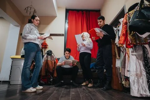 Young performers backstage discussing a script surrounded by costumes Stock Photos