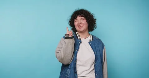 Young person in denim jacket gesturing with finger against blue background .. Stock Footage 313951565