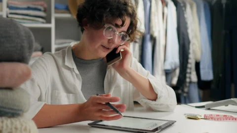Young person multitasking with a phone and tablet while organizing clothes i Stock Footage 323717163