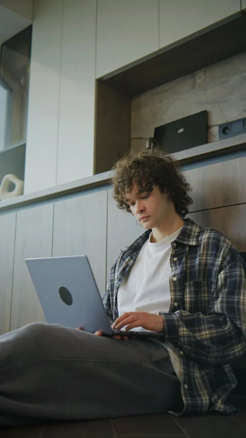 Young person sits on floor using laptop in modern room with wooden walls and she Stock Footage 344924451