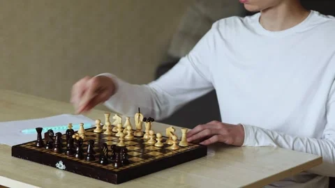 A young person sits at a table, making a move on a chess board Stock Footage 278900222