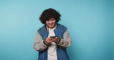 Young person smiles while using phone against blue background in a studio s.. Vídeo Stock 328247713