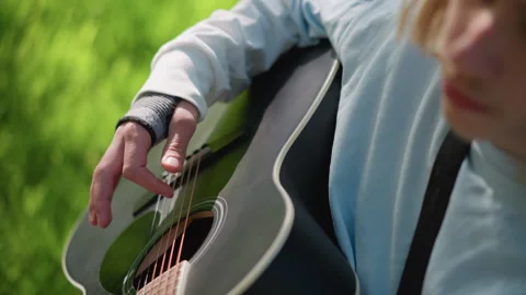 Young person strumming acoustic strings in peaceful park setting. Close shot of Stock Footage 327987006