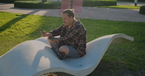 Young Person Using Smartphone While Relaxing On Modern Outdoor Bench... Stockbeeldmateriaal 333525066