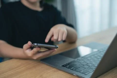 Young person using smartphone while pointing at laptop keyboard on wooden d.. Stock Photos