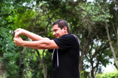 Young peruvian man warming up by stretching arms before exercise. Stock Photos