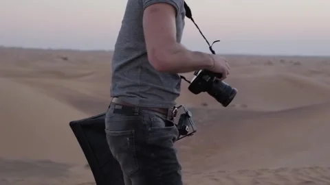 A young photographer with a camera in his hands stands barefoot through the sand Stock Footage 246273106