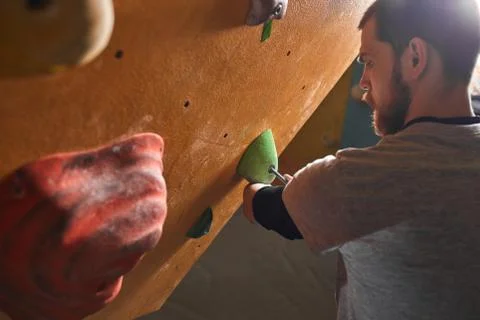 Young physically challenged rock-climbing trainer inspecting and fixing holds Stock Photos