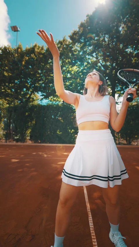 Young player practices serve on red clay tennis court under clear blue sky at Stock Footage 338243355