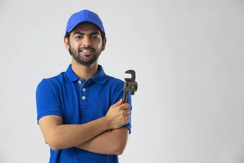 A YOUNG PLUMBER SMILING AT CAMERA WHILE HOLDING HIS TOOL	 Stock Photos