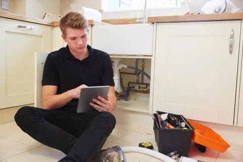 Young plumber with tablet computer fixing sink in kitchen Stock Photos