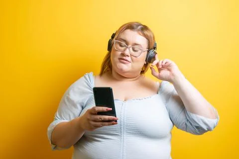 Young plus size Caucasian model listening to music with headphones from her m Photos