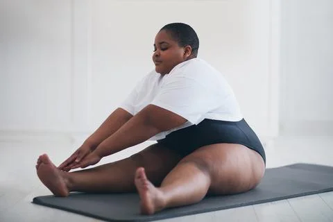 Young plus size woman does stretching exercises on sport mat at home, muscule Stock Photos