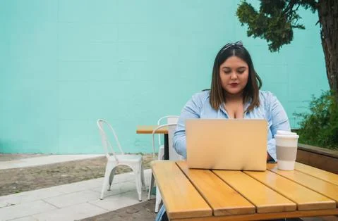 Young plus size woman using laptop at coffee shop. Stock Photos