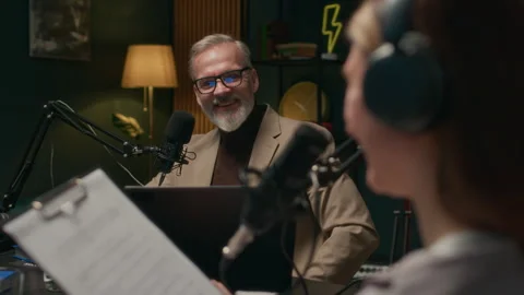 Young Podcaster Reading Script while Talking to Mature Guest during Interview Stock Footage 309325455