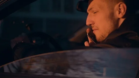 A young positive guy talks briskly on the phone in his car and hears good news Stock Footage 89009883