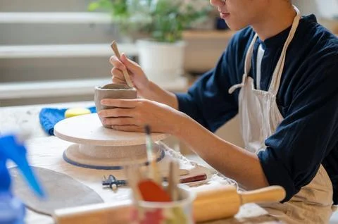 Young pottery artist using a throwing tool to make clay mug at working tabl.. Stock Photos