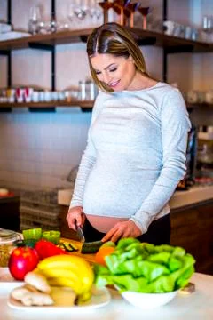 Young pregnant girl cutting vegetables and fruits Stock Photos