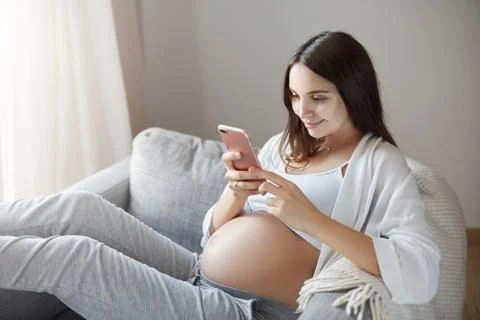 Young pregnant lady using smart phone to get all the status updates of her Stock Photos