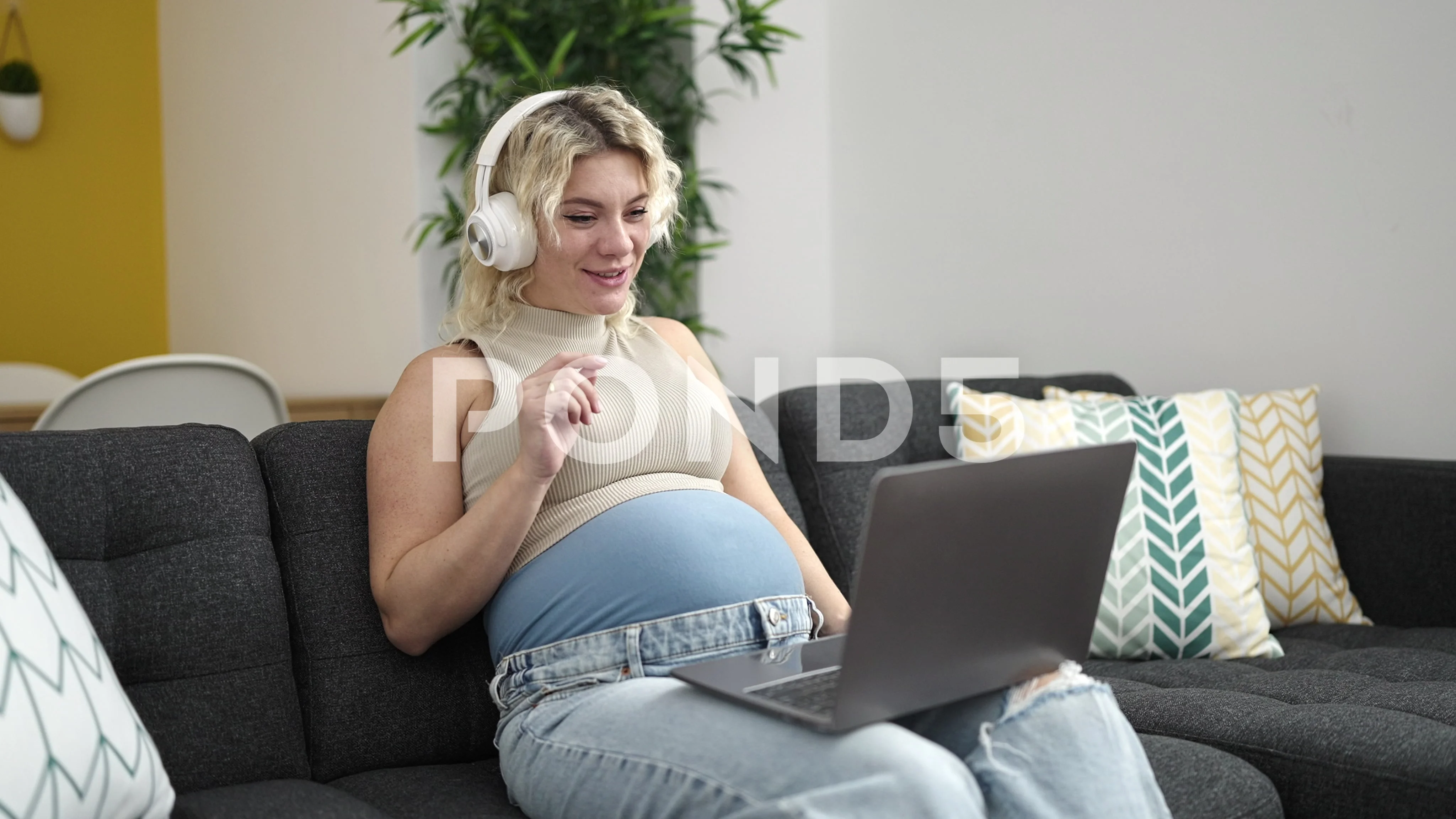 Young pregnant woman having video call touching belly at home