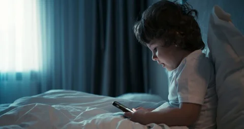 Young pretty boy sitting in white bed and search something on the phone. 4K Stock Footage 113405307