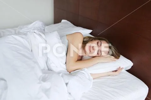 Young pretty girl sleeping in morning on wooden bed with white linens. Stock Photos