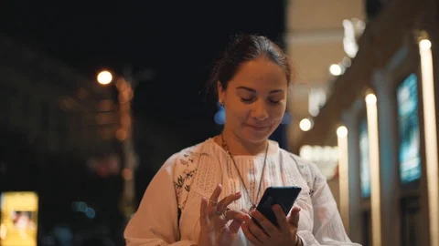 Young pretty girl using mobile phone or smartphone on night city street with Stock Footage 112795545