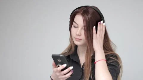 Young pretty lady in black wireless headphones uses smartphone, light background Video stock 137540973