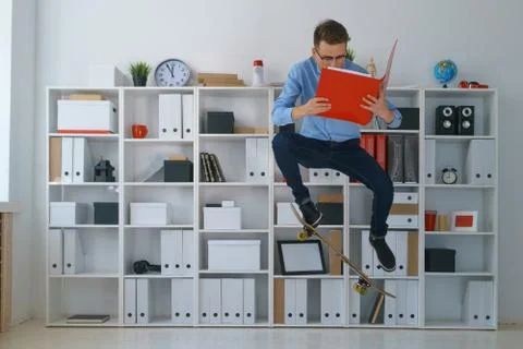Young pretty man work at office hold binder ride on skateboard Stock Photos