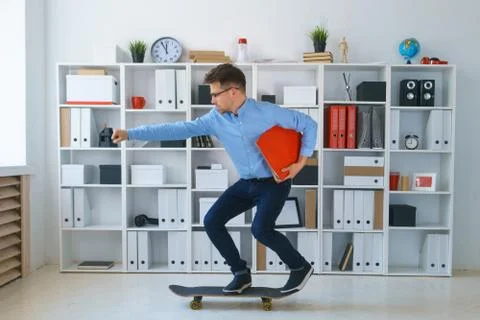 Young pretty man work at office hold binder ride on skateboard Stock Photos
