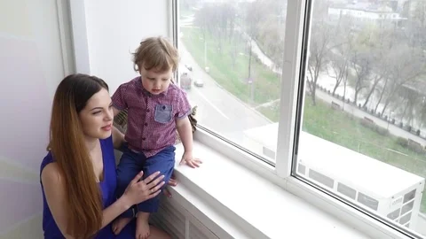 Young pretty mother looking to the window with her baby boy son slow motion Stock Footage 74634330