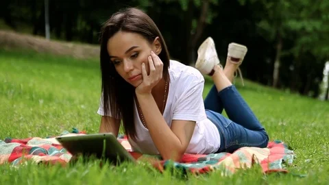 The young pretty slender dark-haired woman using digital tablet in a park. HD 動画素材 76085638