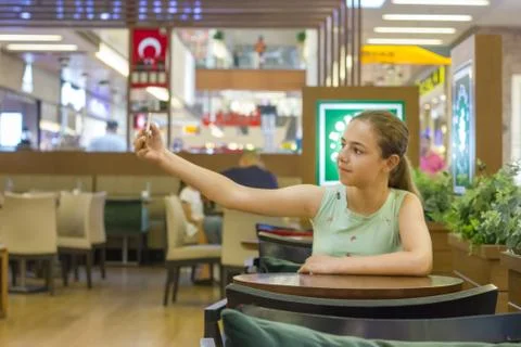 Young pretty teenager girl takes selfie in a cafe at shopping mall Stock Photos