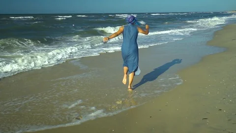 Young pretty woman fun runs along the seashore. She's happy. Sandy beach and sea Stock Footage 98953053