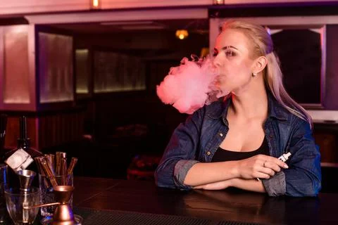 Young pretty woman smoke an electronic cigarette at the vape bar Stock Photos