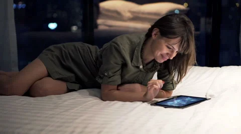 Young, pretty woman using tablet computer while lying on bed at night 動画素材 60736449