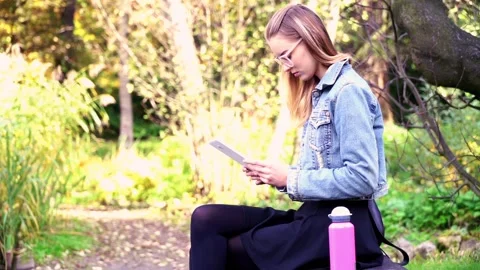 Young, pretty woman using tablet while sitting in beautiful garden Stock Footage 85817736