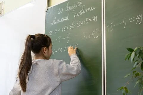 A young primary school student writes complex mathematical equations on a g.. Stock Photos