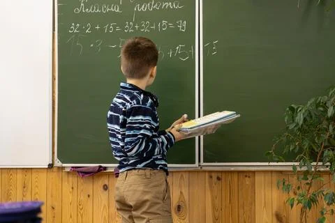 A young primary school student writes complex math exercises on a green cha.. Stock Photos