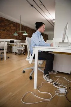 Young professional in beanie working on computer at modern office desk, cop.. Stock Photos