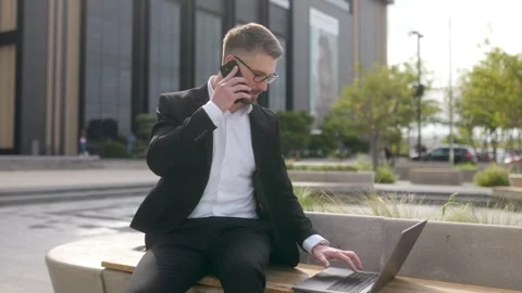 Young Professional on Bench Typing on Laptop While Communicating on Phone Stock Footage 286137431