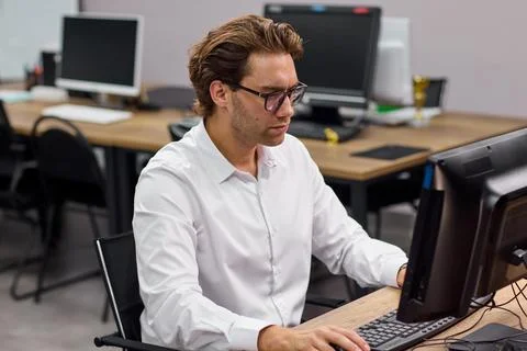 Young professional man typing at desktop computer in modern office training room Stock-Fotos