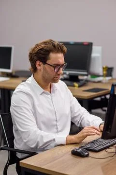 Young professional man typing at desktop computer in modern office training room Stock-Fotos