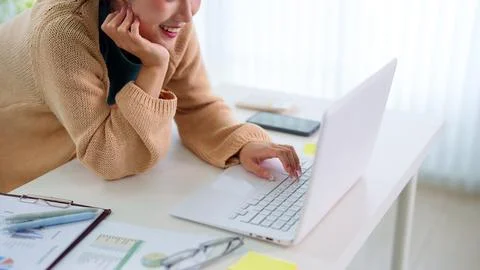 Young professional using laptop at bright modern desk while taking phone ca.. Stock Photos