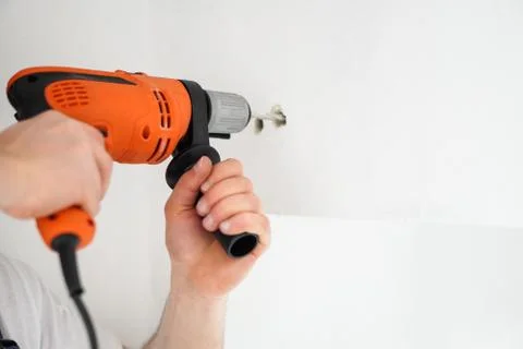 Young professional worker with drill making a hole in white wall. Stock Photos