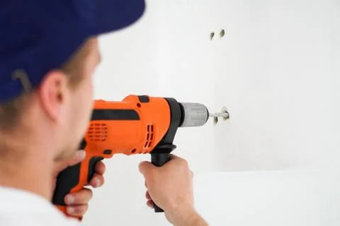 Young professional worker with drill making a hole in white wall. Stock Photos