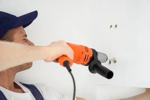 Young professional worker with drill making a hole in white wall. Stock Photos